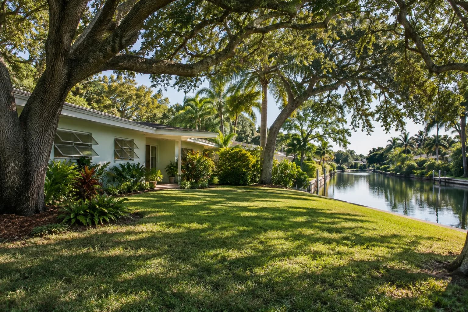 A Plantation ranch home shaded by large trees beside a canal