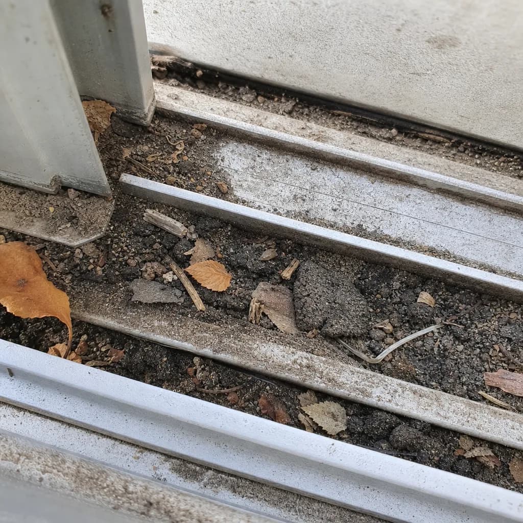 A sliding door track packed with dirt and debris before cleaning