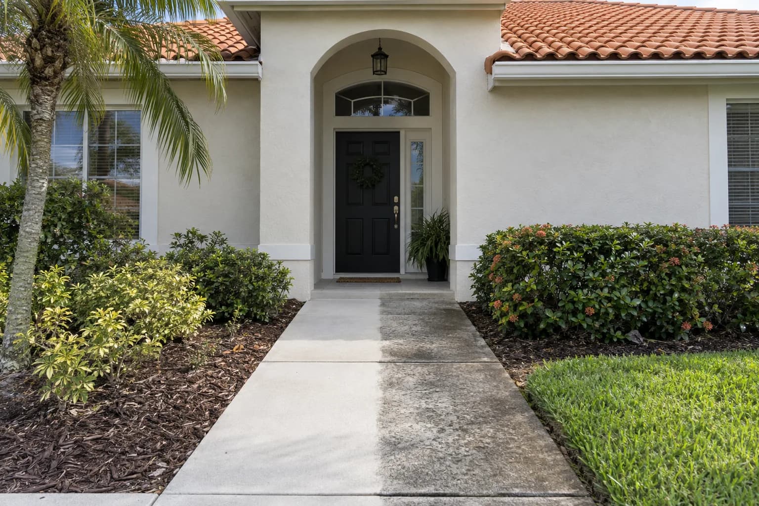 A driveway being pressure washed beside a stucco wall that has been soft washed